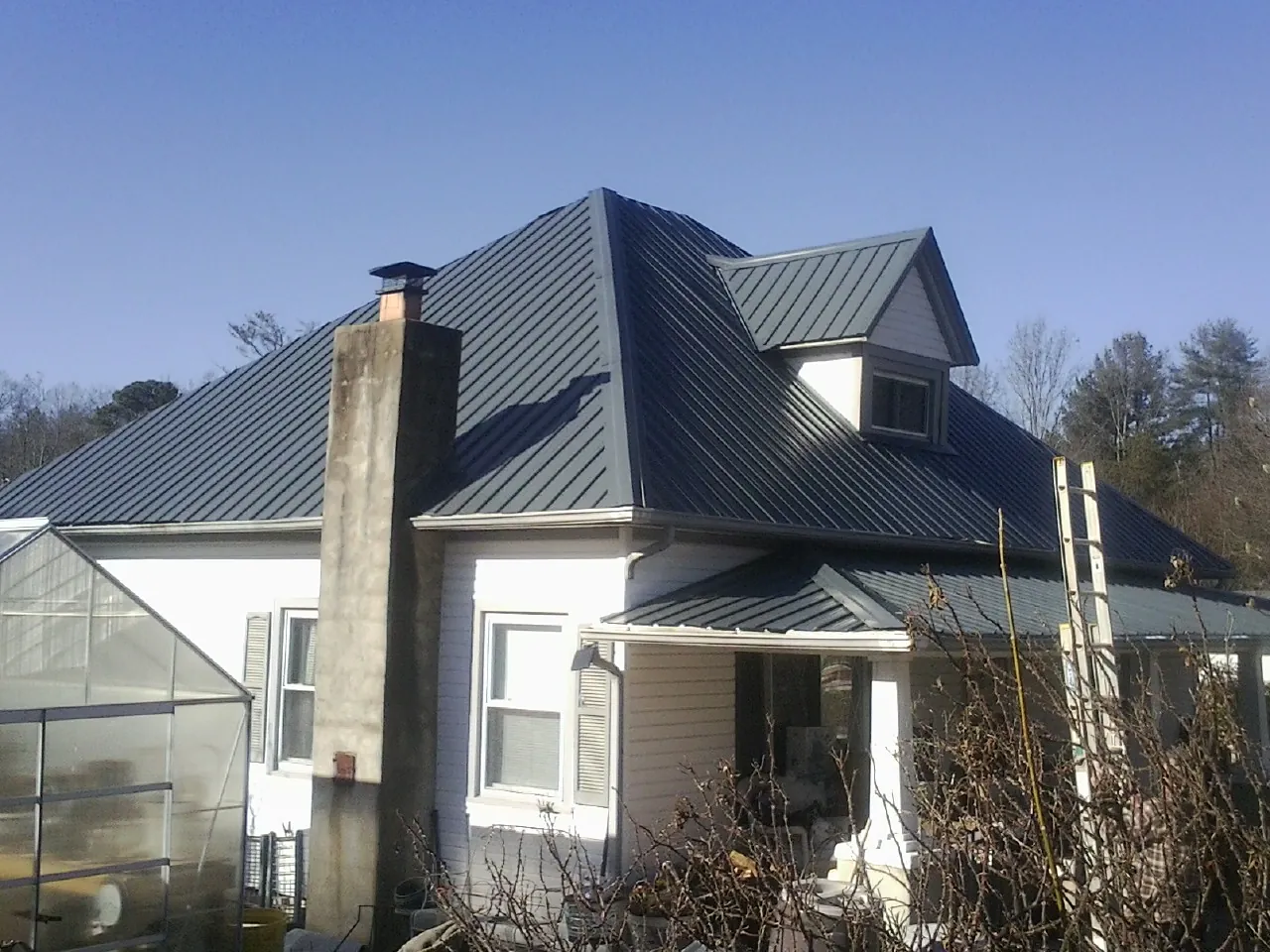 Dark blue standing seam metal roof on a white farmhouse with dormer — Slate & Tile Roof Repair by Roofing Brothers in Gueydan