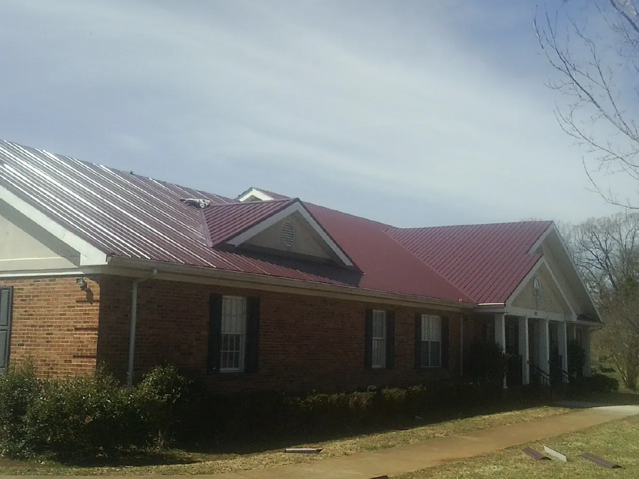 Red metal roof with gabled entries on a long brick building, from a Hail Damage Roof Repair job in Gueydan