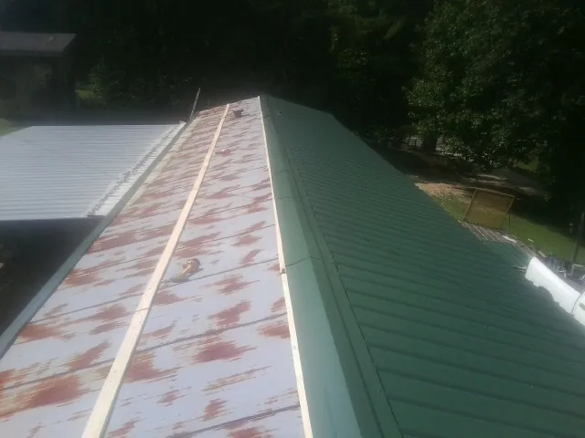 Old rusted panels beside newly installed green metal roofing — Wind Damage Roof Repair by Roofing Brothers in Gueydan