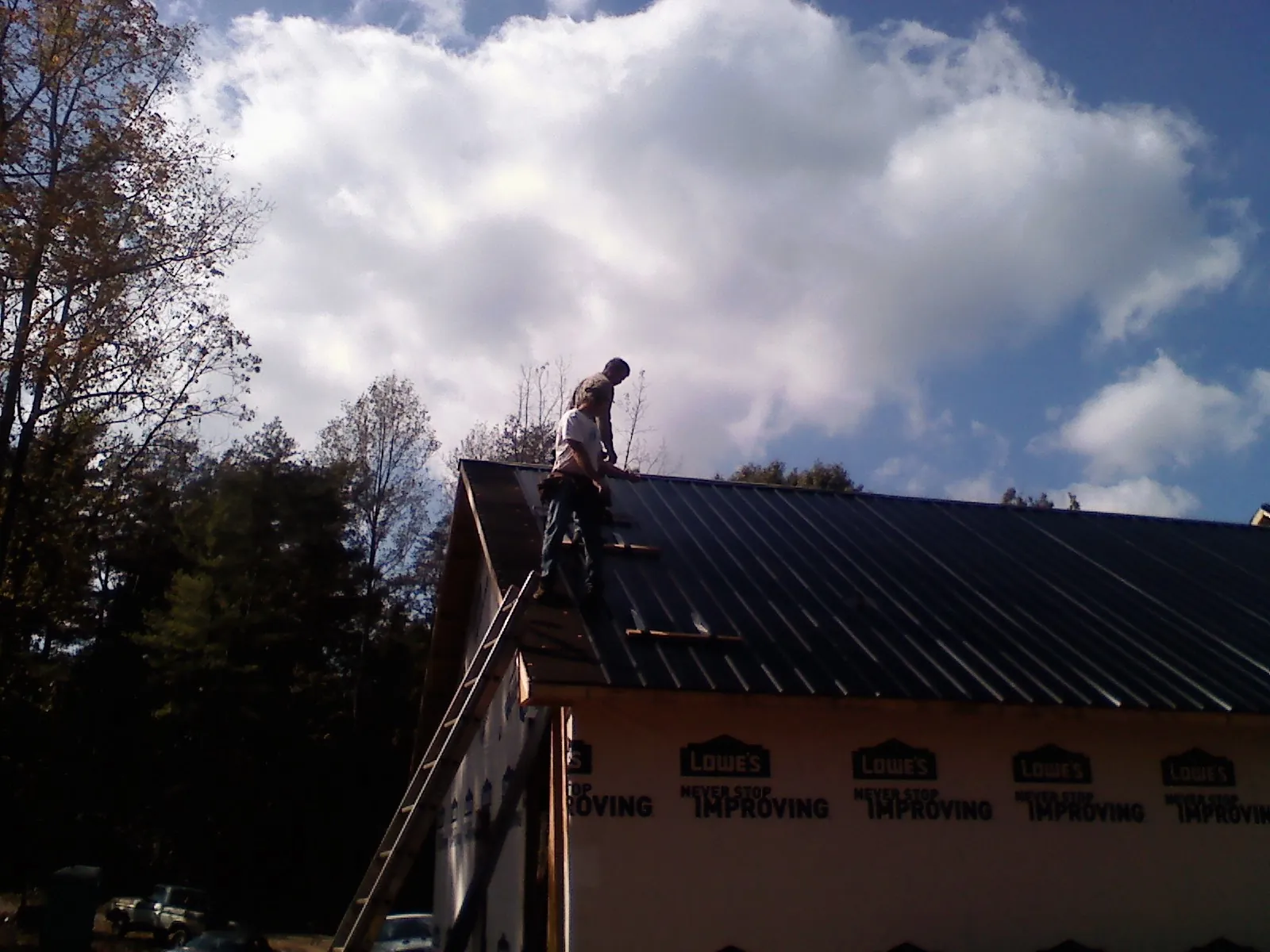 Roofer fastening dark metal panels high against a cloudy sky, from a Roof Inspection job in Gueydan